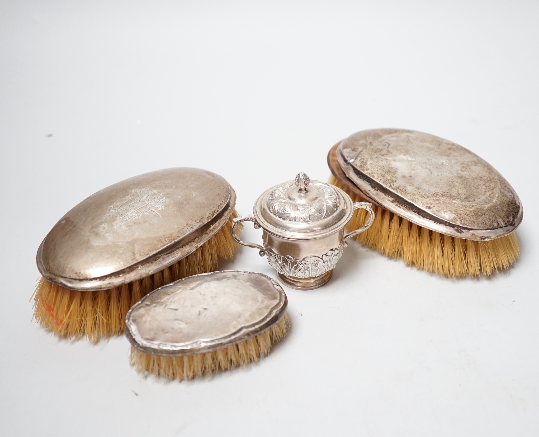 A small George V silver twin handled cup and cover, London, 1929 and three silver mounted brushes.